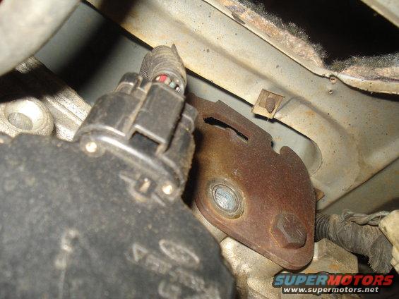 Close-up of a black electrical connector and rusty metal bracket attached to vehicle engine components