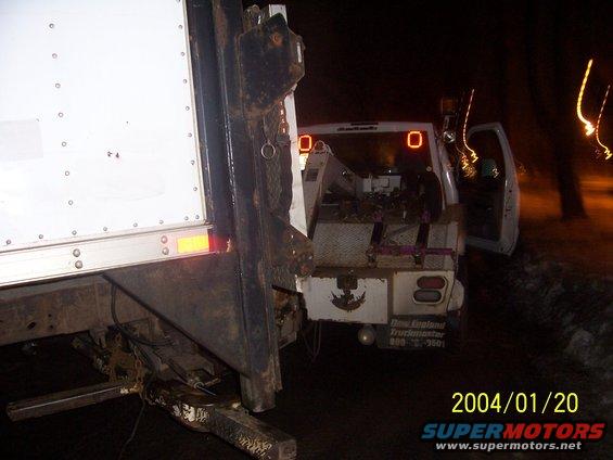 Tow truck bed loaded with equipment, parked next to a white box truck at night
