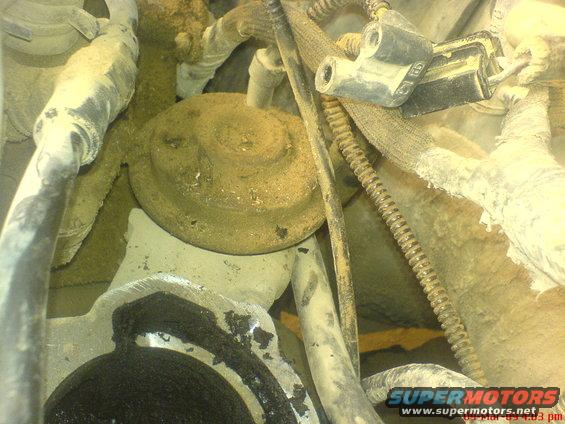 Close-up of engine parts covered in dirt, with hoses and wiring visible