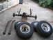 1991 Ford Bronco - A disassembled front axle assembly, leaf springs, and tires are laid out on a paved surface, likely for a vehicle repair or upgrade.