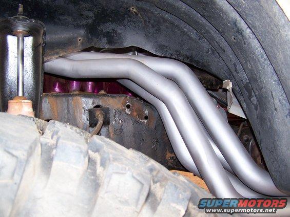 Exhaust headers and suspension components visible near a large tire
