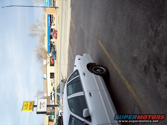 white sedan parked in lot, other cars and buildings in background