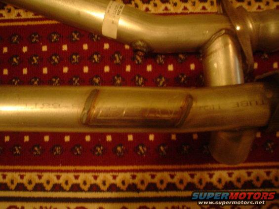 Two silver exhaust pipes with visible welds, resting on a patterned rug