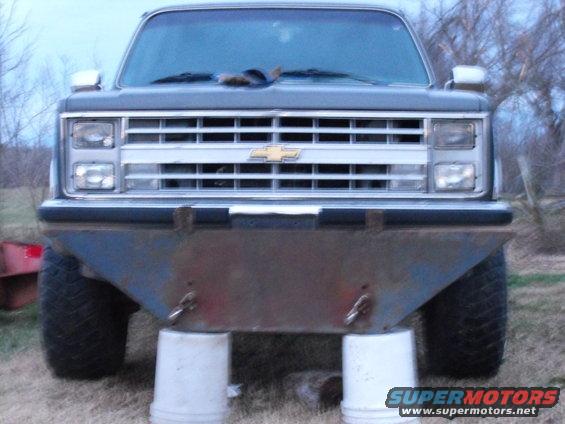 Front view of a dark-colored Chevrolet truck with a custom bumper, supported by buckets