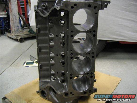 Gray engine block with cylinder bores visible, resting on cardboard in a garage
