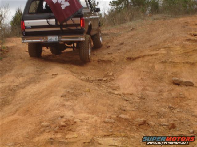 Brown SUV with a maroon flag in the back, driving on a dirt hill