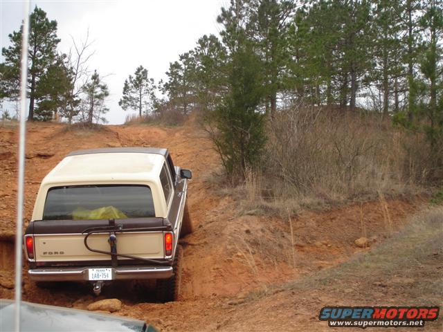 Tan and brown Ford Bronco with a yellow tarp in the back, driving on a dirt hill