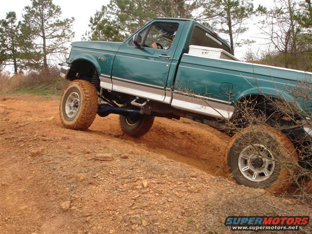 Green pickup truck with lifted suspension on a dirt trail