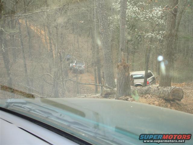 Two SUVs navigating a muddy, wooded trail. One is partially obscured by trees