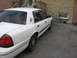 2003 Ford Crown Victoria - A white sedan is parked in front of a brick building with a driveway.