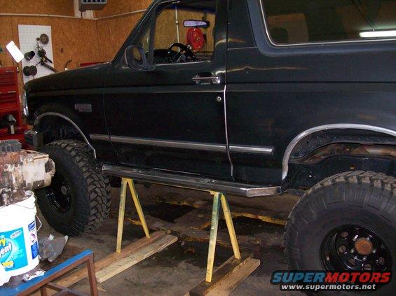 Dark green 1992 Ford Bronco on jack stands in a garage, showing side profile and large tires