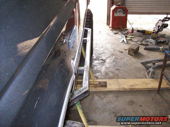 Dark SUV side with custom metal rock sliders, jack stands, and welding equipment in background