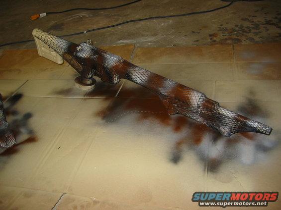 Vehicle part with camouflage pattern being spray painted, resting on cardboard
