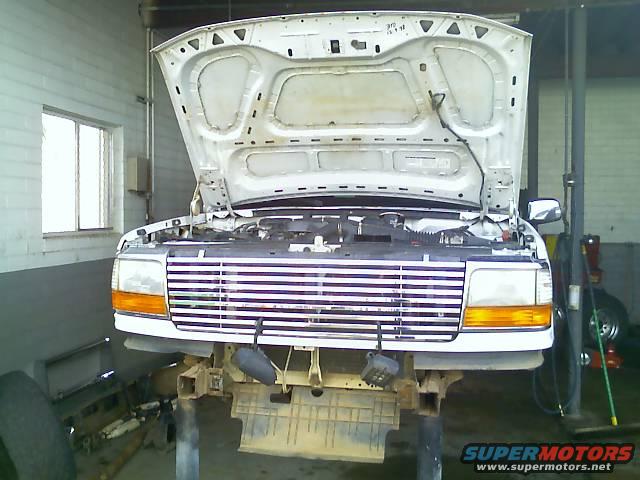 Front of a white Ford F-Series truck with hood open, on a lift in a garage