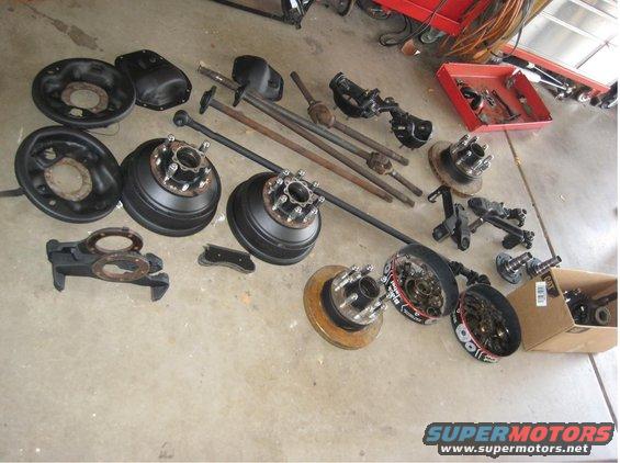 Axles, brake drums, and hubs laid out on concrete floor. Some parts have SuperMotors branding