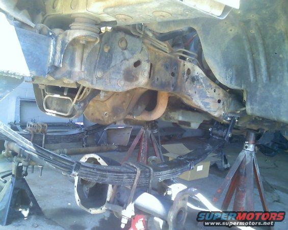 Undercarriage of a vehicle on jack stands, showing leaf springs and differential