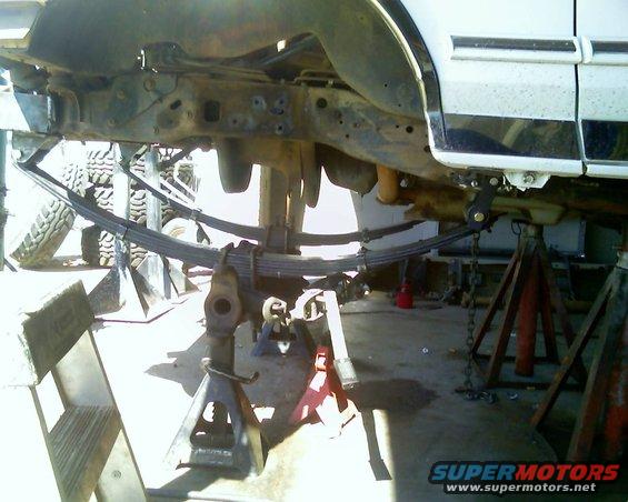 Undercarriage of a white vehicle on jack stands, showing leaf springs and suspension