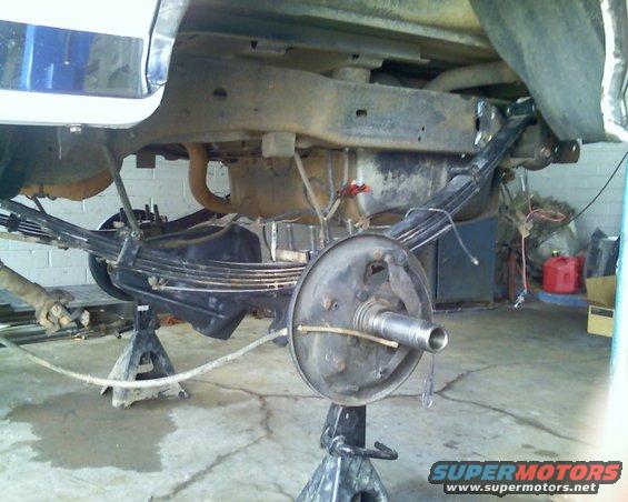 Underside of a vehicle on jack stands, showing the rear axle, leaf springs, and brake drum