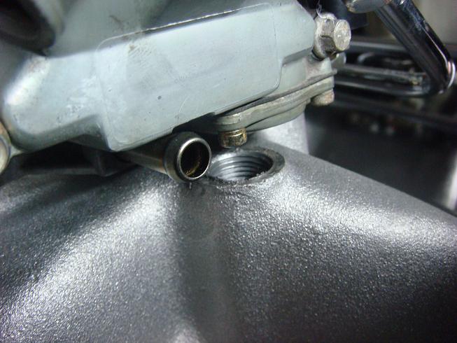 Close-up of a metal fitting on a carburetor with a fuel line attached