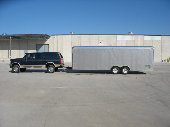 Dark green SUV with tan trim towing a silver enclosed trailer
