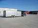 1995 Ford C-350 (Centurion Conversions) - A Ford F-350 pickup truck tows a large silver enclosed trailer in an industrial area under a clear blue sky.