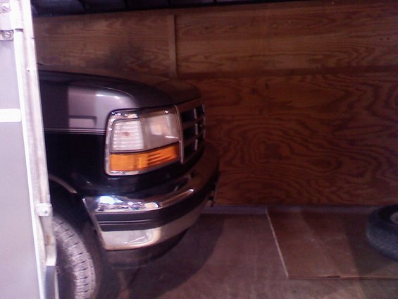 Front corner of a dark-colored Ford F-Series truck, likely from the early to mid-1990s, parked inside a trailer or garage