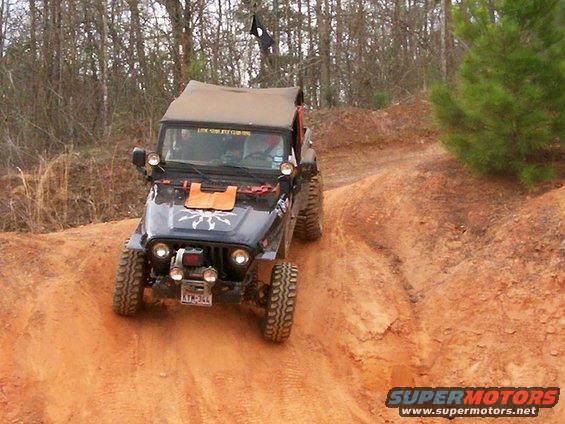 Black Jeep Wrangler TJ with tan soft top on dirt trail