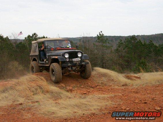 Black Jeep CJ-7 with tan soft top driving on a dirt hill