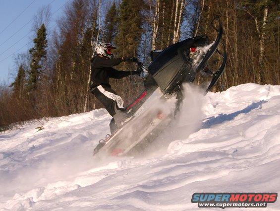 Snowmobile kicking up snow on a slope, rider wearing helmet and dark clothing