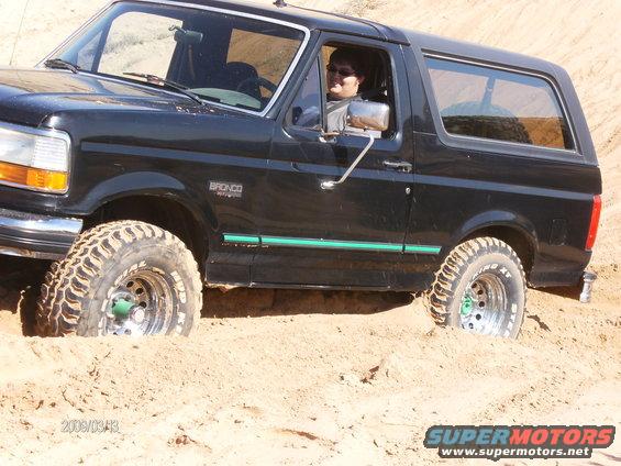 Black 1993 Ford Bronco stuck in sand with driver visible