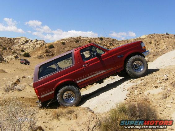 Red Ford Bronco climbing a dirt hill, with another red SUV in the background