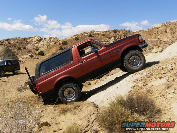 Red 1993 Ford Bronco climbing a dirt hill, another black Bronco in background