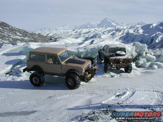 Two modified off-road vehicles parked on ice with mountains in the background