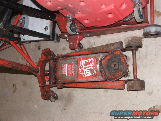 Red and silver Snap-on 2 Ton floor jack with visible wear and tear, resting on a concrete floor