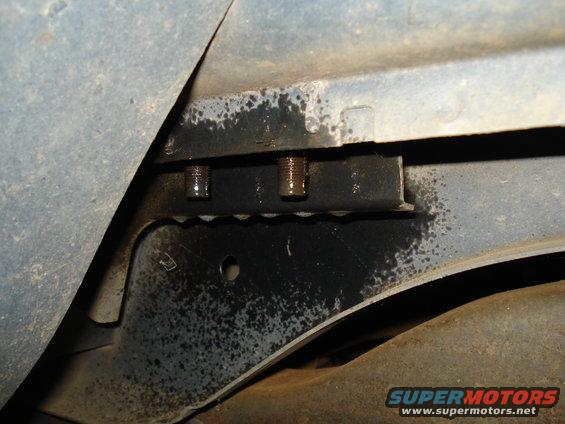 Close-up of two bolts on a black bracket with oil residue underneath a vehicle.