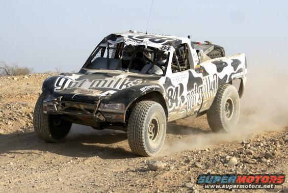 Modified off-road truck with roll cage and large tires driving on dirt