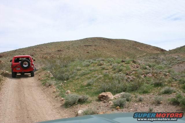 Red SUV driving on a dirt road in a desert landscape