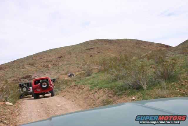 Red SUV with spare tire on rear door, followed by black SUV on dirt road