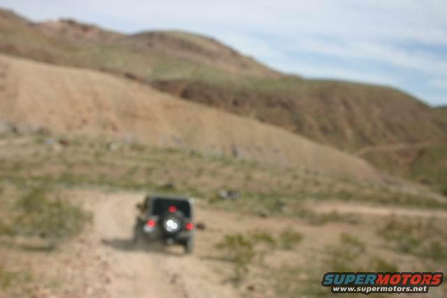 Jeep Wrangler driving on a dirt road in a desert landscape