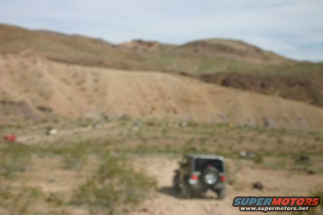 Dark gray Jeep Wrangler driving on a dirt road in a desert landscape