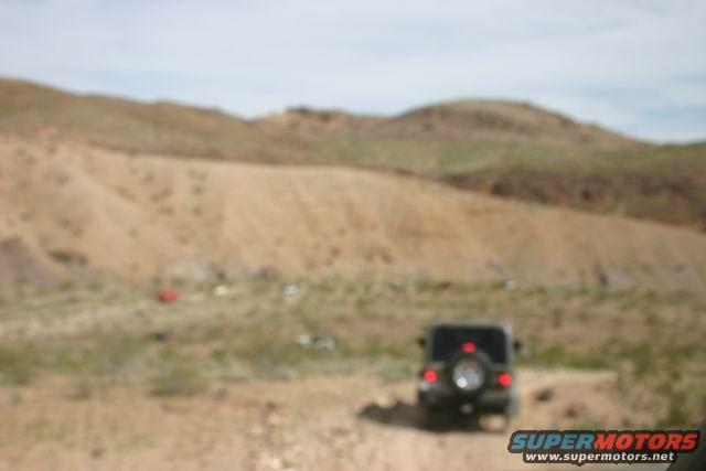 Black SUV with spare tire on rear door, seen from behind in a desert landscape