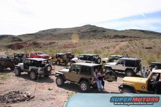 Several Jeeps parked in a desert area with hills in the background