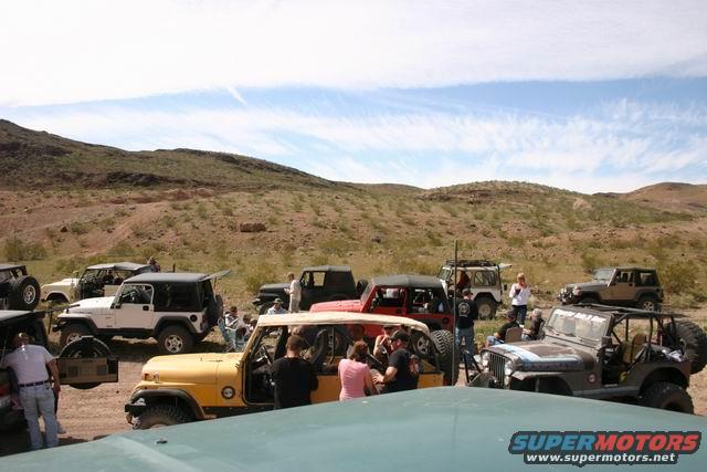Several Jeeps parked in a desert landscape with people around them