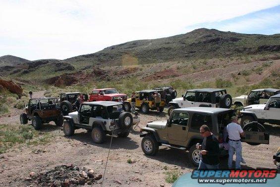 Several Jeeps parked on a dirt road in a desert landscape with hills in the background