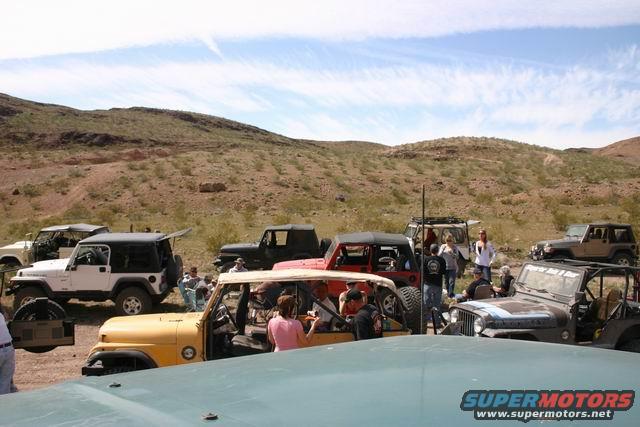 Several Jeep SUVs parked in a desert landscape with people standing around