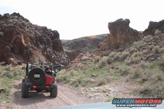 Rear view of Jeep Wrangler with spare tire and red gas can on off-road trail