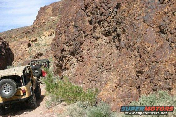 Two off-road vehicles driving on a narrow dirt trail through a rocky canyon