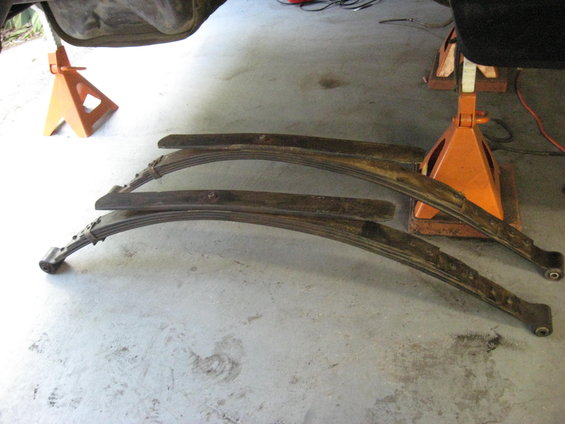 Two rusty leaf springs resting on a concrete floor under orange jack stands