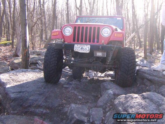 Red 2003 Jeep Wrangler with lifted suspension and large tires navigating a rocky trail