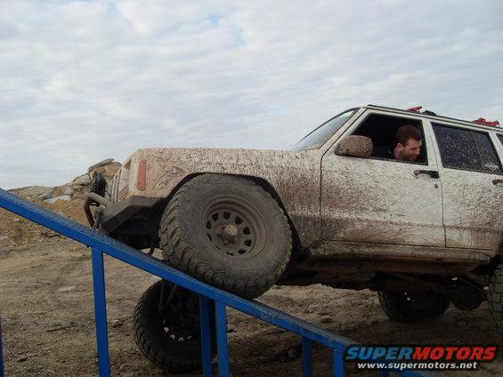 Mud-covered Jeep Cherokee XJ driving up a blue ramp on an off-road course